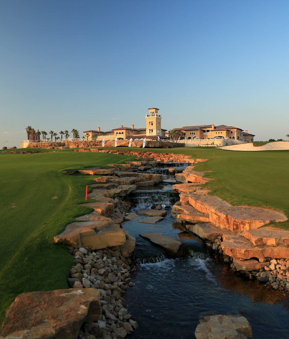 Farbspektakel bei DP World Tour Championship 2023. Der Earth Course der Jumeirah Golf Estates präsentiert sich nach einigen Neuerungen auf und abseits der Fairways in starken Farben: gleißendes Weiß, schillerndes Rot, sattes Grün. Hier die Abschlussbahn, das Par 5 mit dem Clubhaus im Hintergrund.
